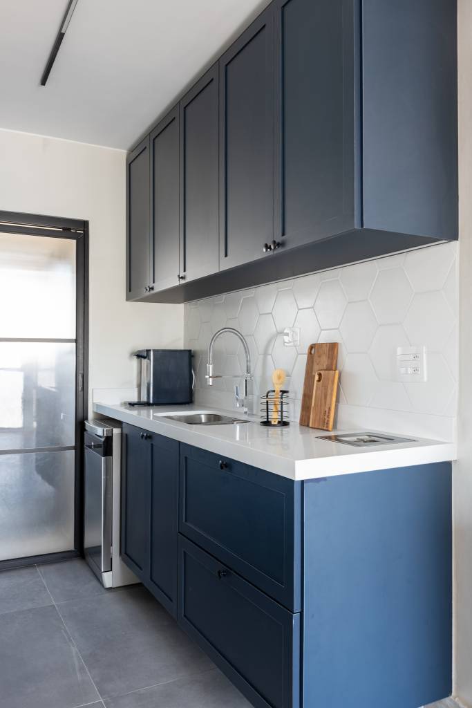 ape-96m-varanda-cara-quintal-ladrilhos-coloridos-estudio-monfre-06-cozinha-azul Cozinha integrada com armários azuis, bancada branca e backsplash de azulejos brancos.