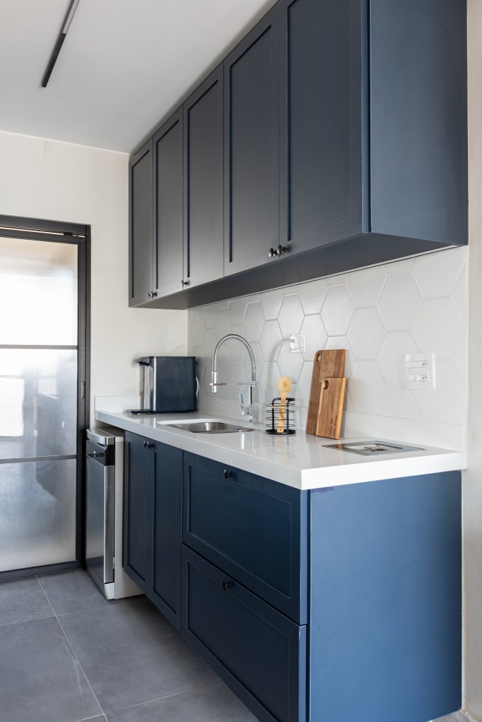 Cozinha integrada com armários azuis, bancada branca e backsplash de azulejos brancos.
