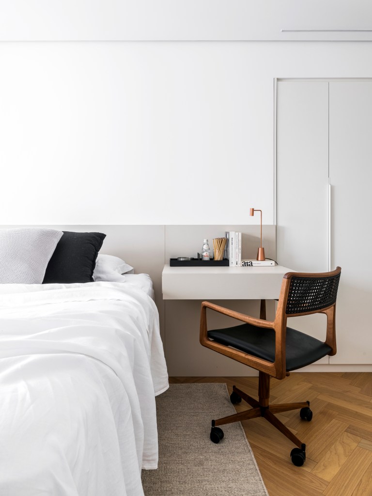 Projeto de Ticiane Lima. Na foto, quarto minimalista com piso de madeira, armário branco e bancada pequena. Penteadeira.