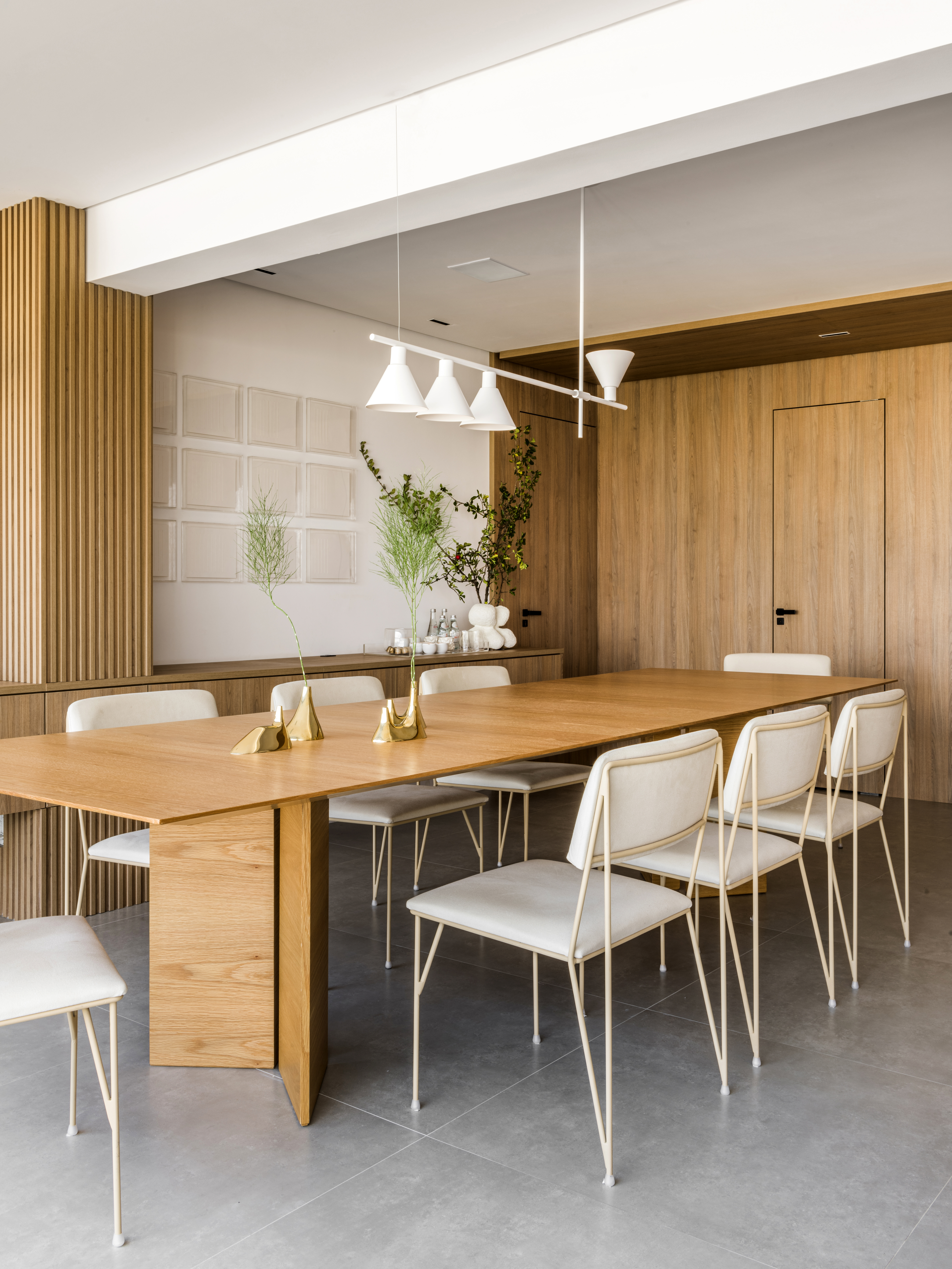 Projeto de Ticiane Lima. Na foto, sala de jantar com mesa de madeira, cadeiras com estofado branco, luminária e buffet de madeira.
