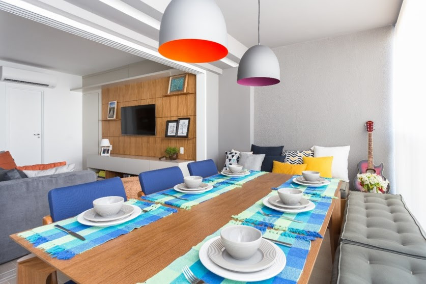 Varanda gourmet com mesa grande de madeira, luminárias coloridas e sofá com futon.