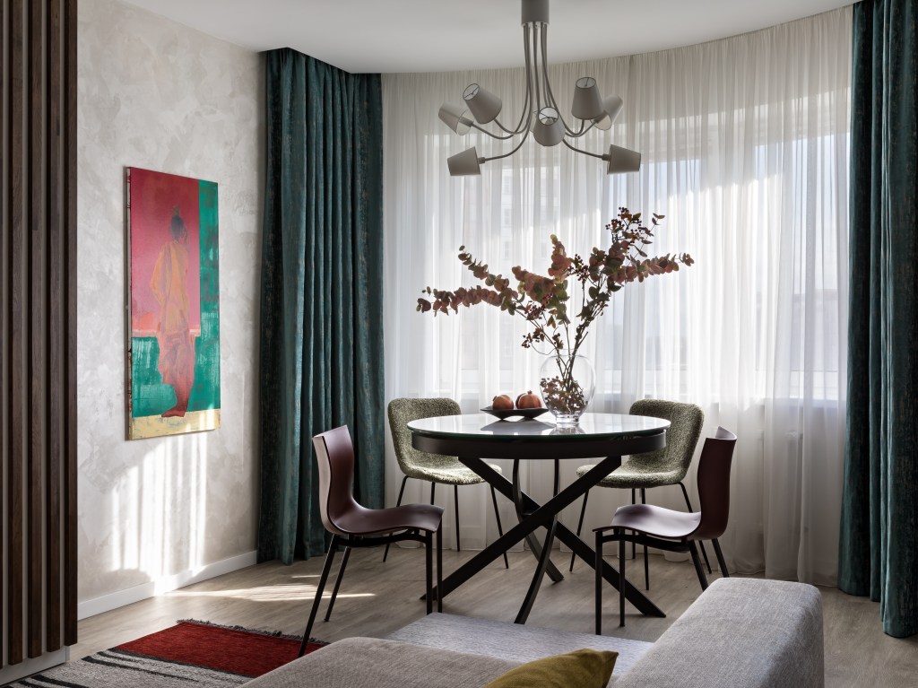 Sala de jantar com mesa redonda, lustre, cortina branca e cortina verde.
