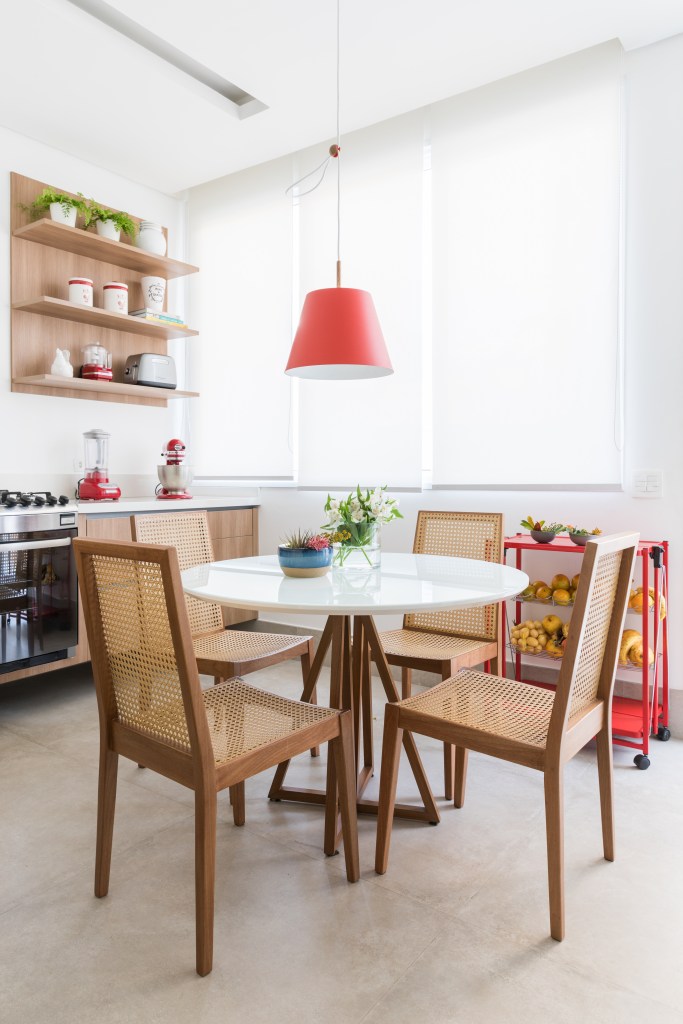 Cozinha com copa; mesa redonda branca, cadeiras de palhinha e luminária vermelha.
