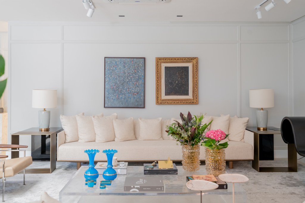 Projeto de Romário Rodrigues Arquitetos. Na foto, sala de estar branca com sofá branco e parede com boiseries e quadros.