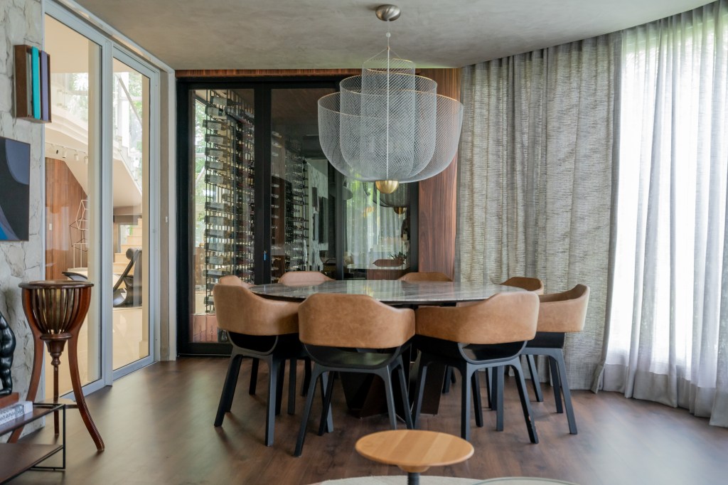 Projeto de Romário Rodrigues Arquitetos. Na foto, sala de jantar com mesa redonda, luminária e adega ao fundo.