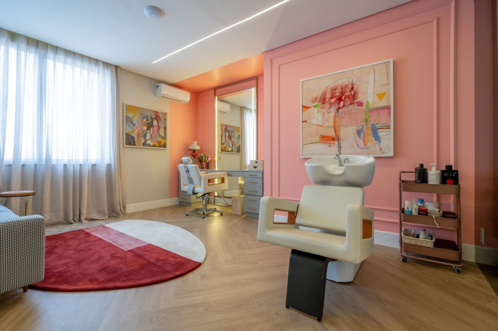 Projeto de Romário Rodrigues Arquitetos. Na foto, salão de beleza rosa com boiseries, cadeira branca e espelho com iluminação lateral embutida.