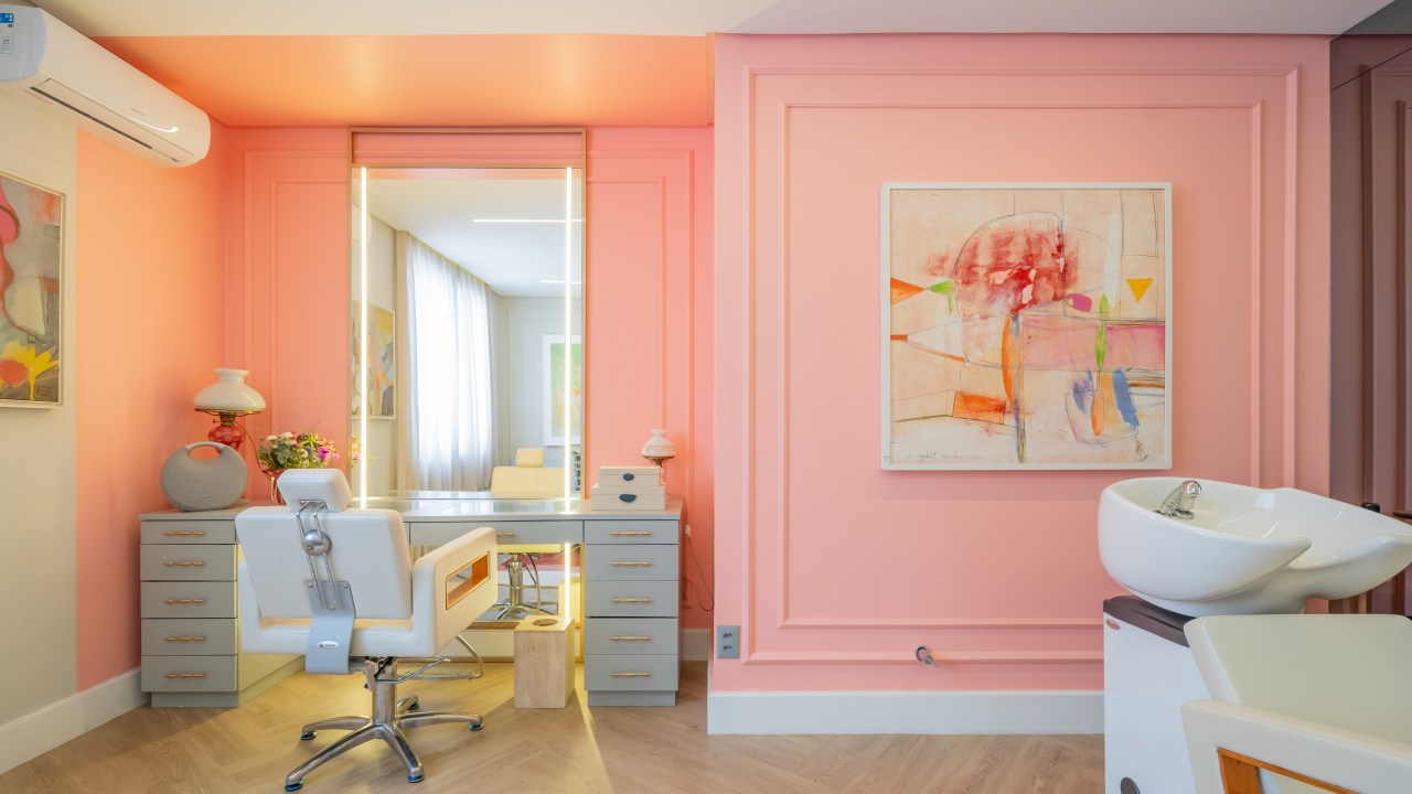 Projeto de Romário Rodrigues Arquitetos. Na foto, salão de beleza rosa com boiseries, cadeira branca e espelho com iluminação lateral embutida.