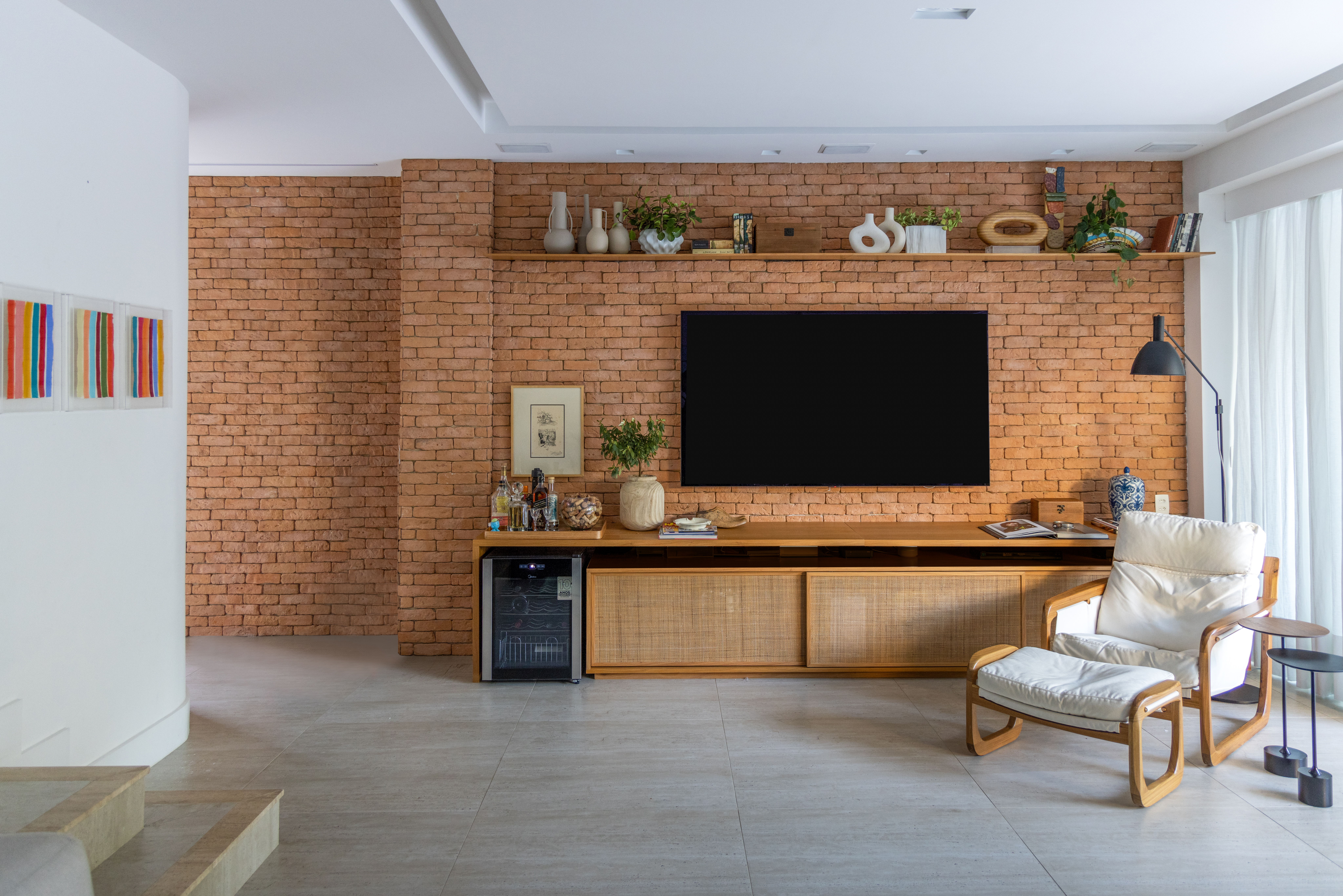 Projeto de Manuela Santos. Na foto, sala de estar com parede de tijolinhos e rack de madeira.