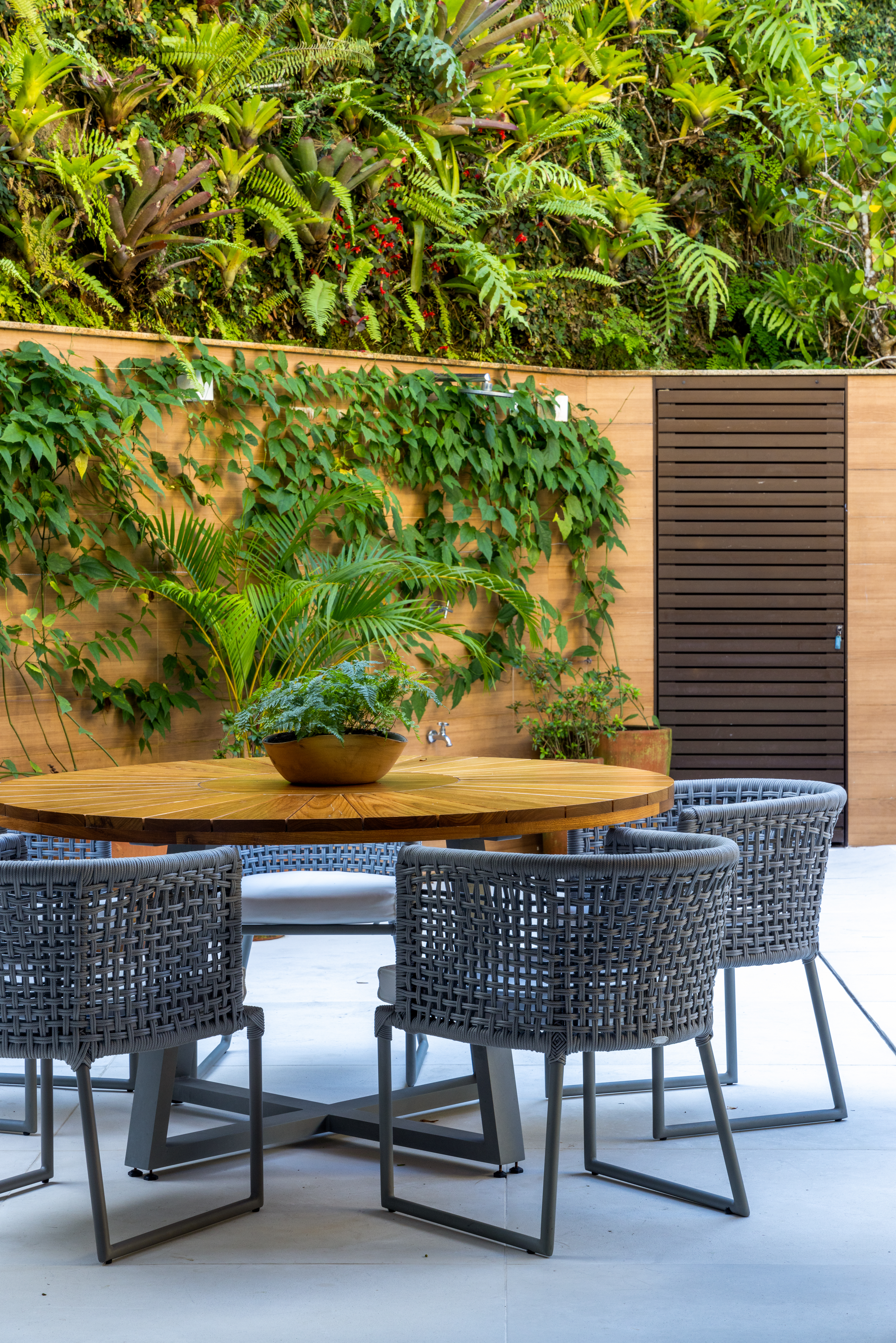 Projeto de Manuela Santos. Na foto, área externa com jardim e mesa redonda de madeira.
