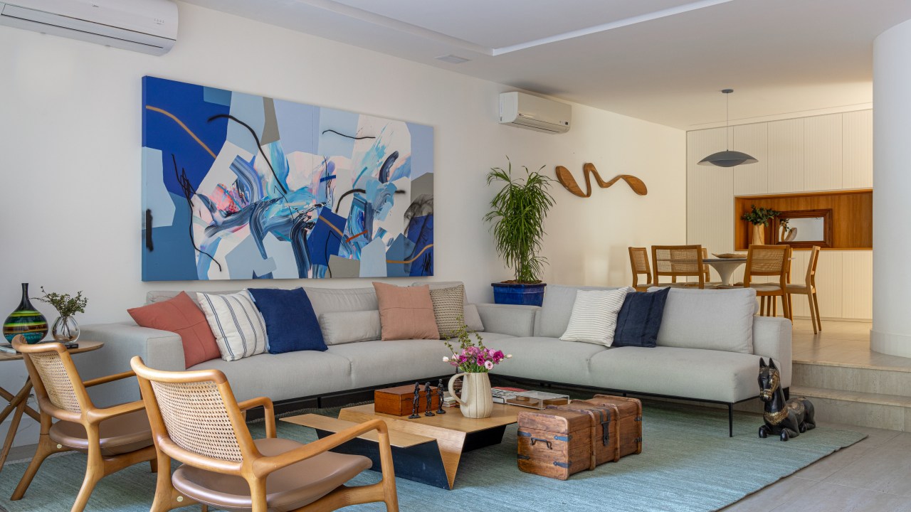 Projeto de Manuela Santos. Na foto, sala de estar com sofá L off white, tapete azul e mesa de centro de madeira.