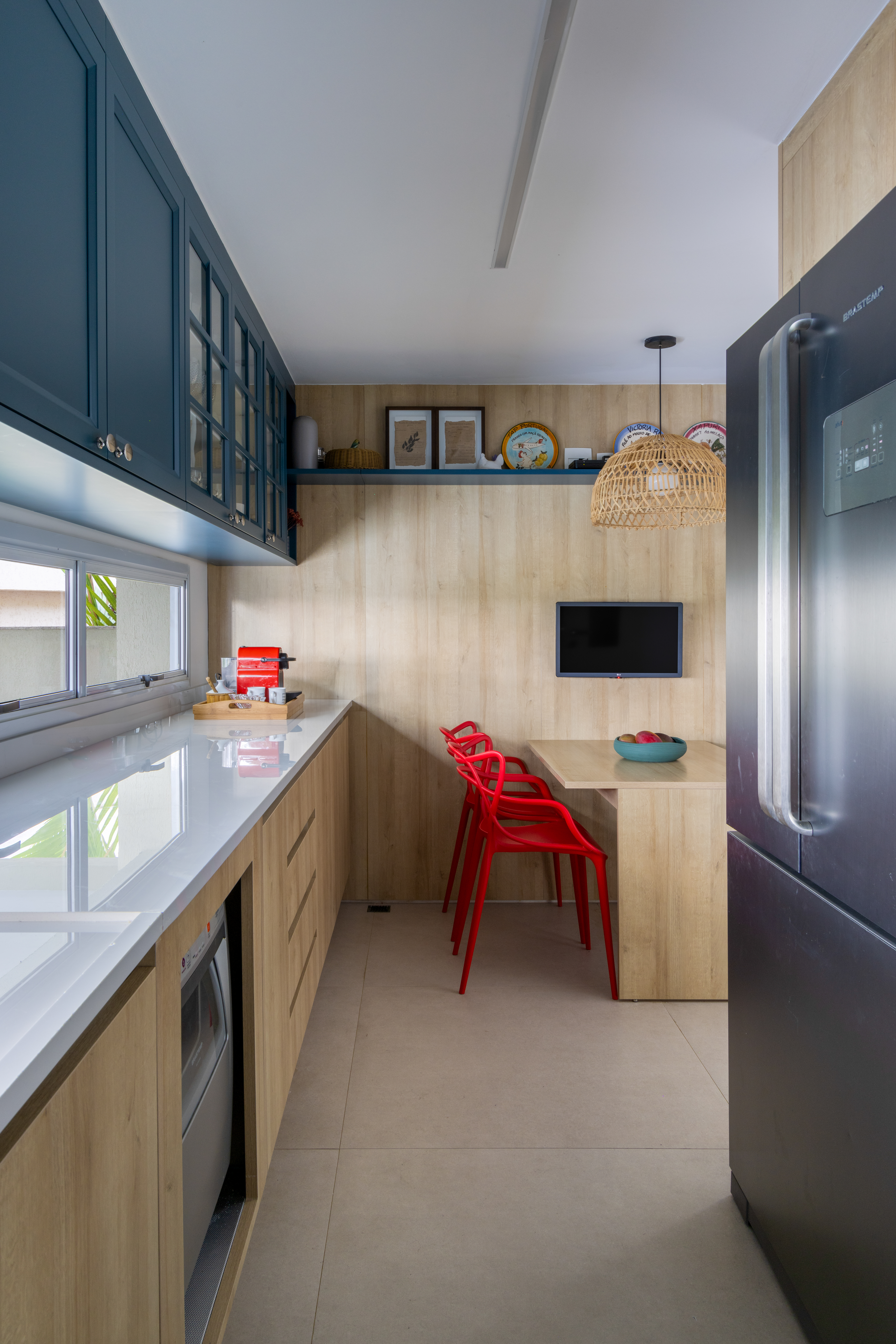 Projeto de Manuela Santos. Na foto, cozinha com paredes revestidas de madeira, armários aéreos com portas de vidro e copa.