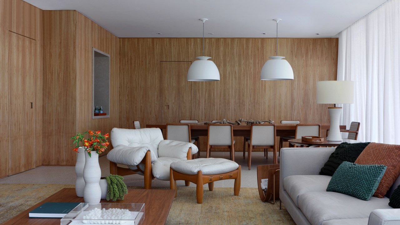 Projeto de Carol Farah. Na foto, sala de estar neutra com sofá cinza, poltrona mole branca e paredes revestidas de madeira.