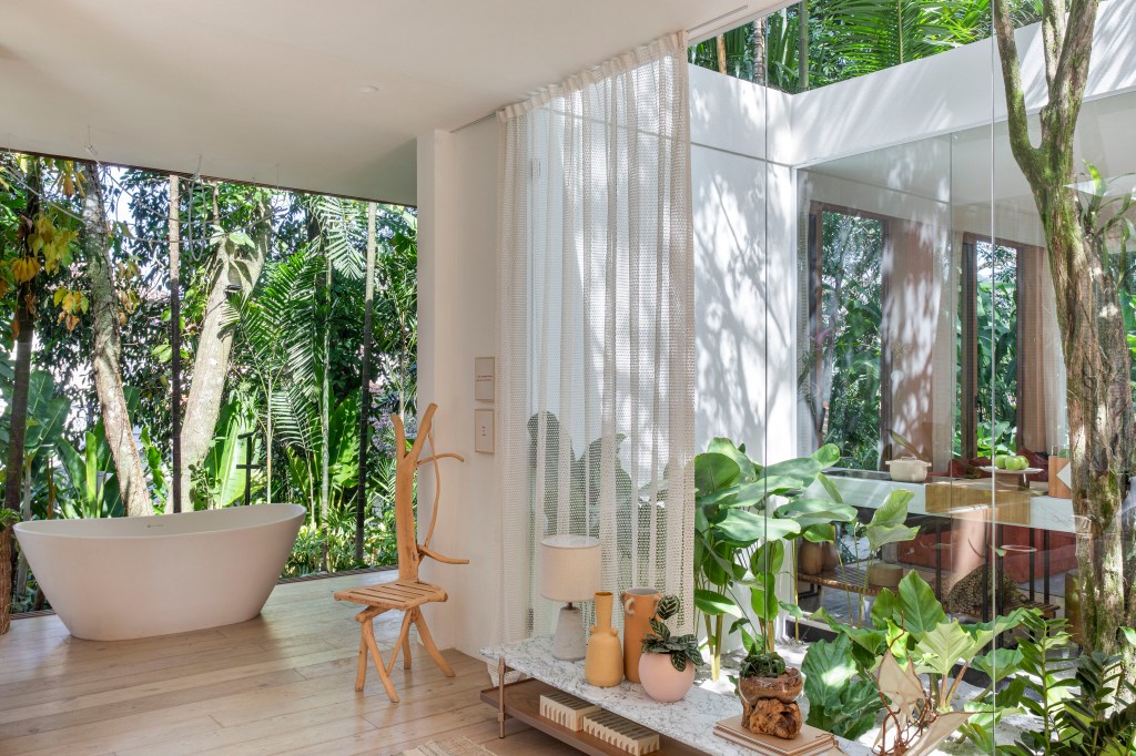 Casa de campo de 105 m² no meio da natureza é feita com três contêineres. Projeto de Up3 Arquitetura para a CASACOR Rio de Janeiro 2023, Na foto, banheiro com banheira, parede de vidro e vista para o jardim.