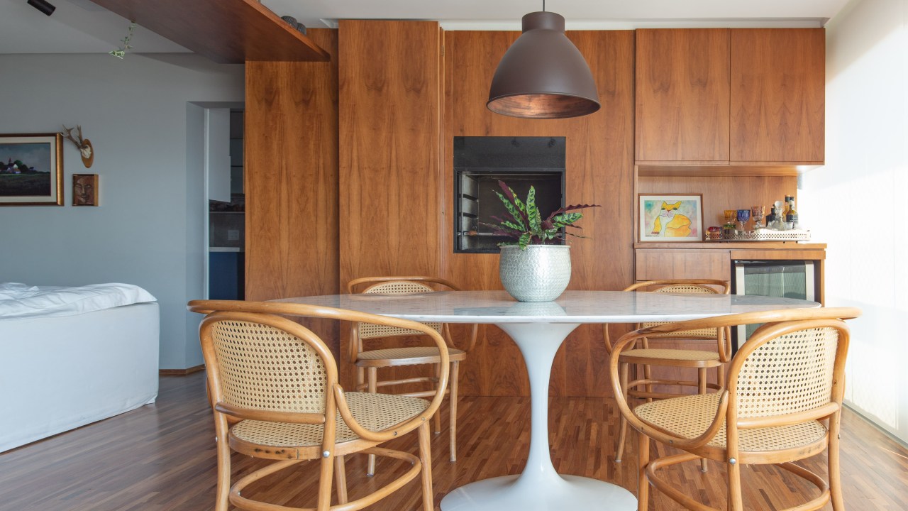 Sala de jantar com paredes revestidas de madeira, mesa branca redonda e cadeiras de palhinha.