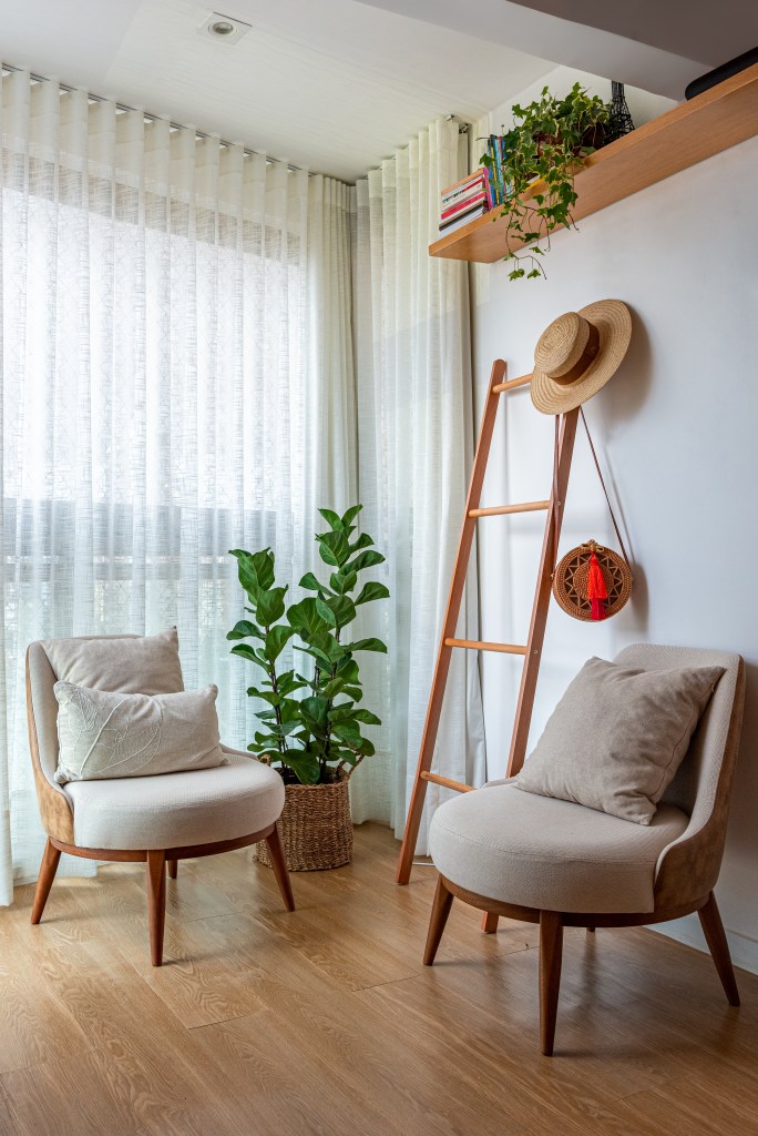 Projeto de Djanira Cabral. Na foto, sala de estar com poltronas claras e escada como cabide.