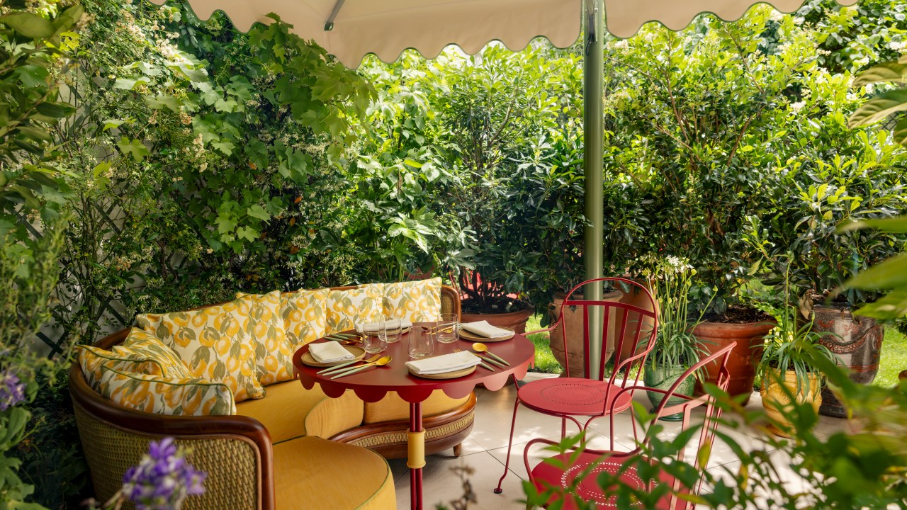 Jardim no terraço com sofá amarelo, mesas, cadeiras e plantas ao redor.