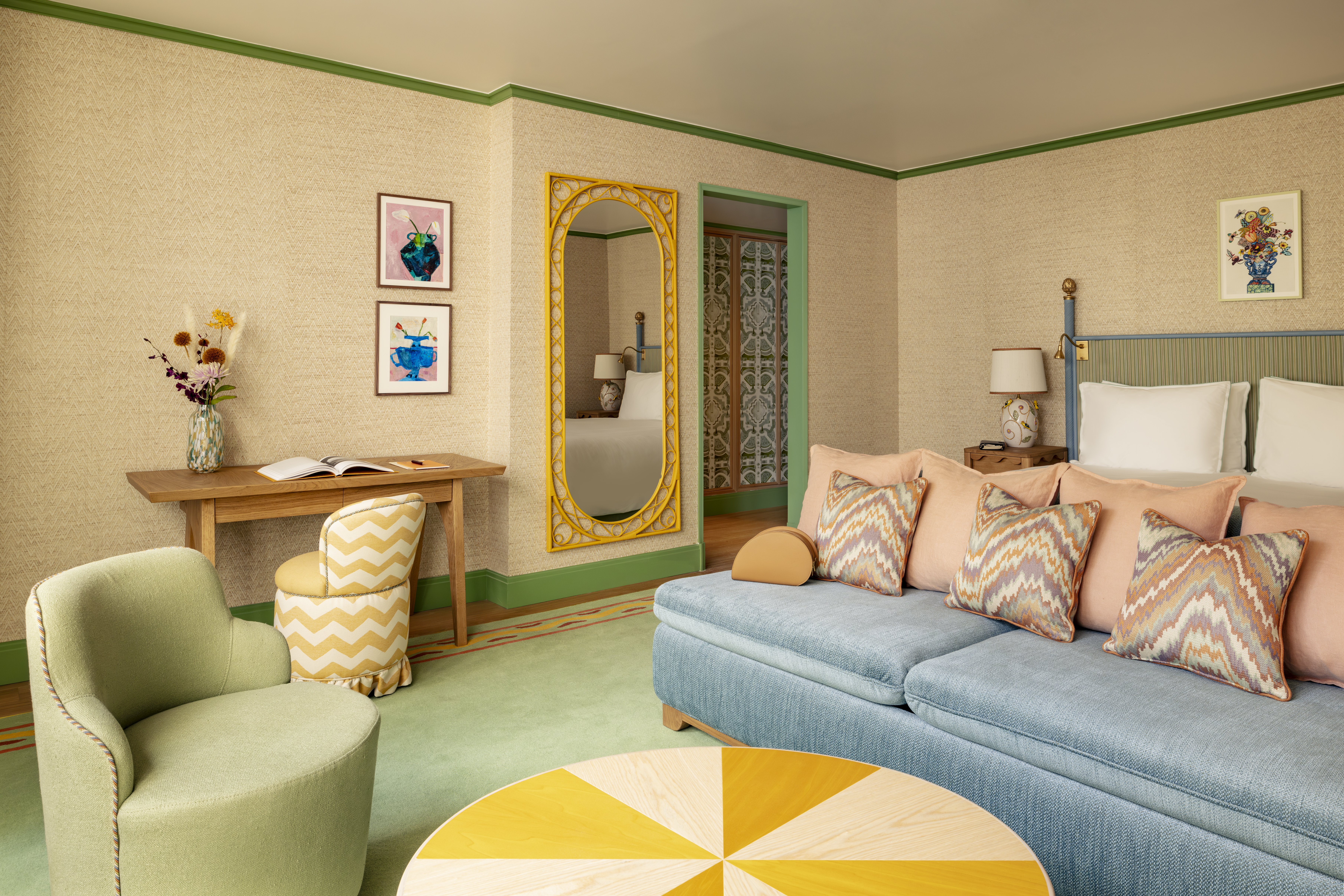 Quarto com piso verde, sofá azul e pufe branco e amarelo.