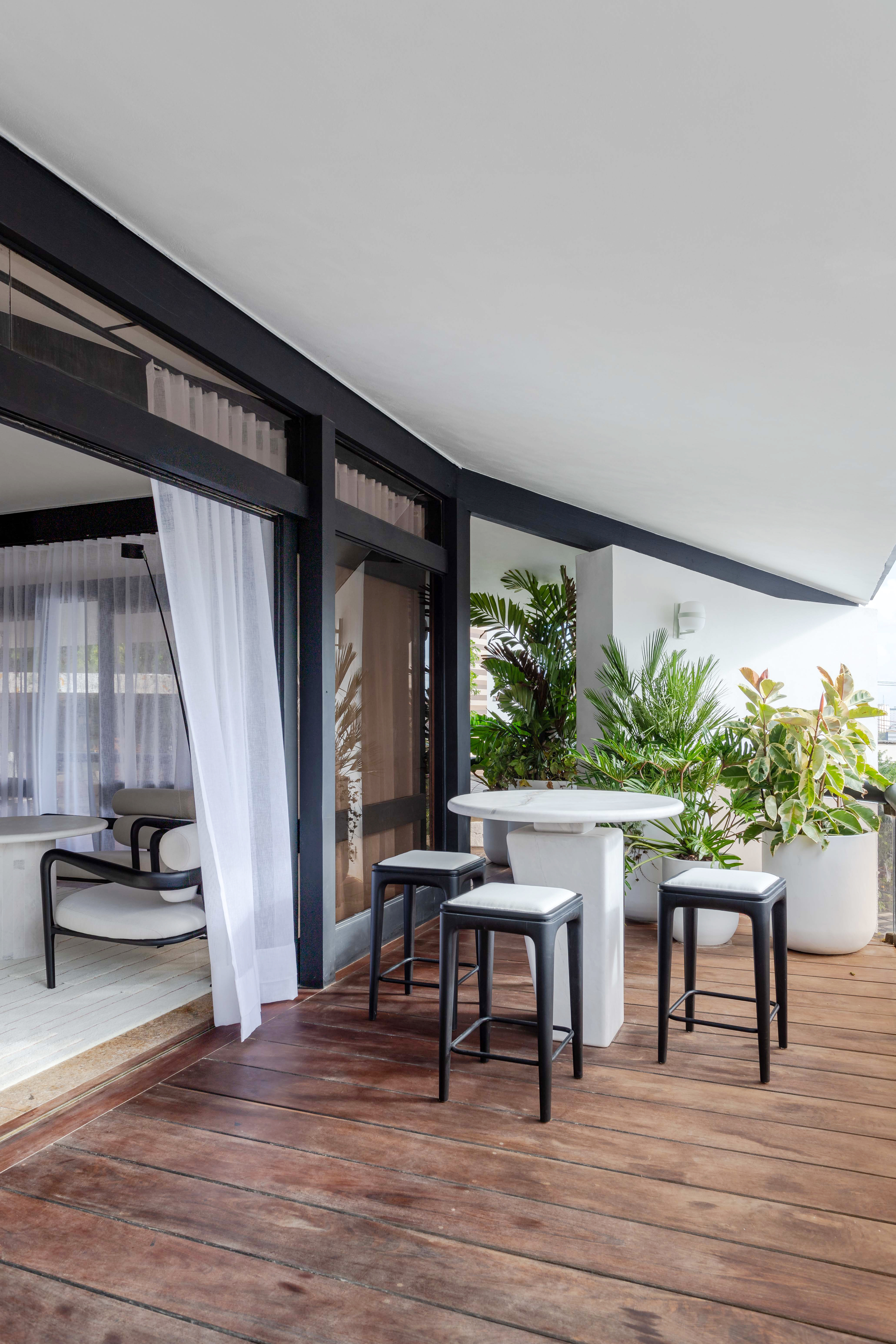 Living minimalista de 85 m² ganha décor em branco, preto, cinza e areia. Projeto de David Bastos para a CASACOR Bahia. Na foto, varanda com mesa de refeições e vasos de plantas.