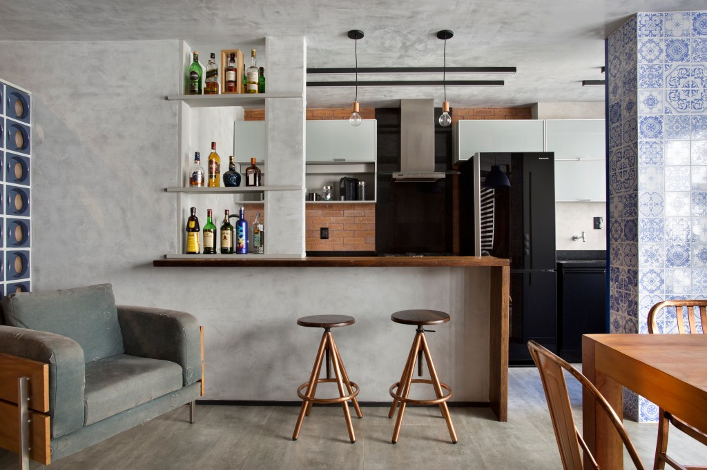 Loft de 70 m² ganha décor industrial inspirado em Nova York. Projeto de Rafael Mirza. Na foto, sala de estar integrada com cozinha, mesa de refeições e parede de cimento queimado.