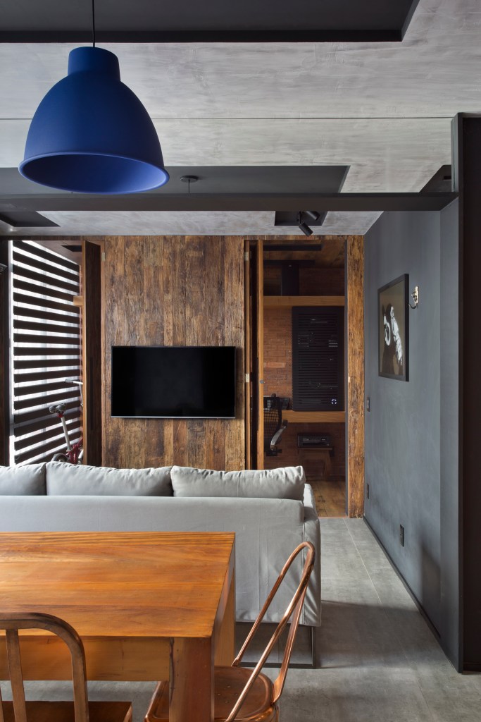 Loft de 70 m² ganha décor industrial inspirado em Nova York. Projeto de Rafael Mirza. Na foto, sala com parede madeira e preta, mesa de madeira e detalhes pretos.