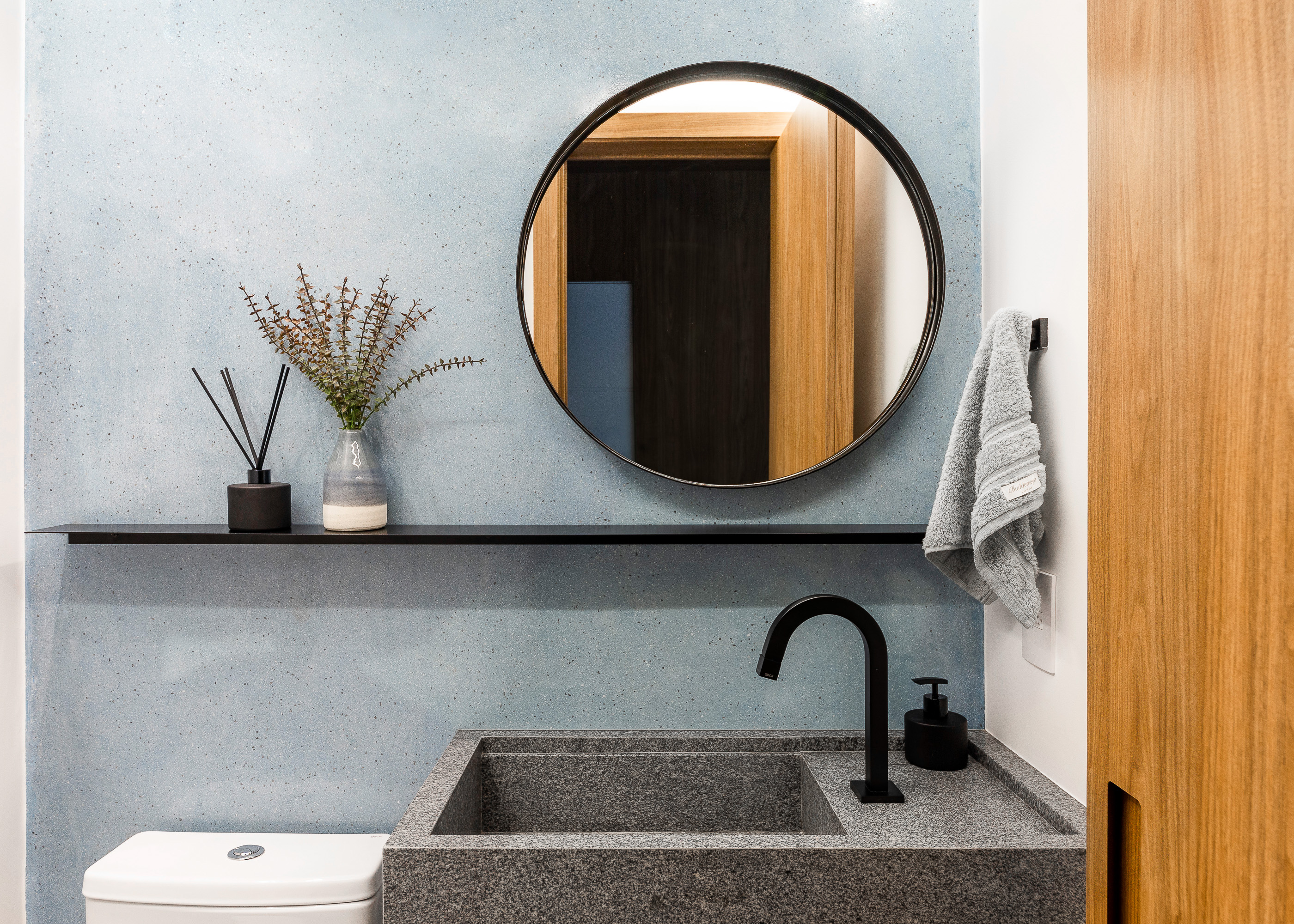 Lavabo com parede azul, espelho redondo e cuba esculpida.