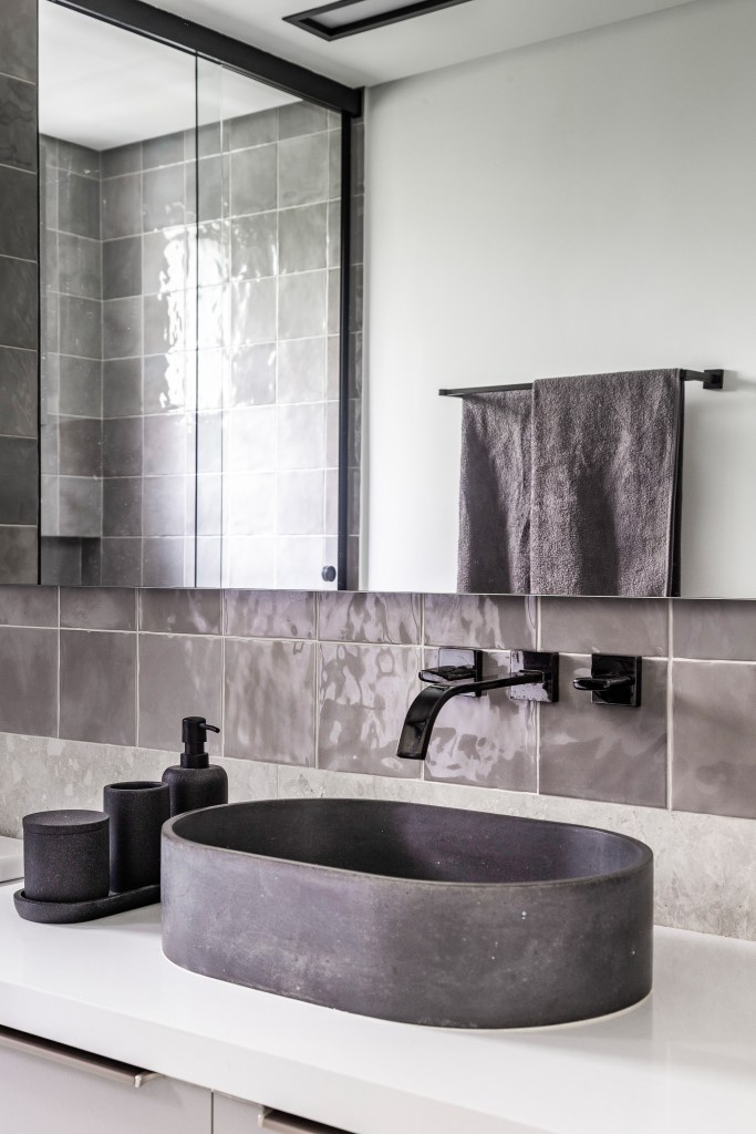 Banheiro com cuba solta cinza em concreto, parede com azulejos cinzas e marcenaria branca.