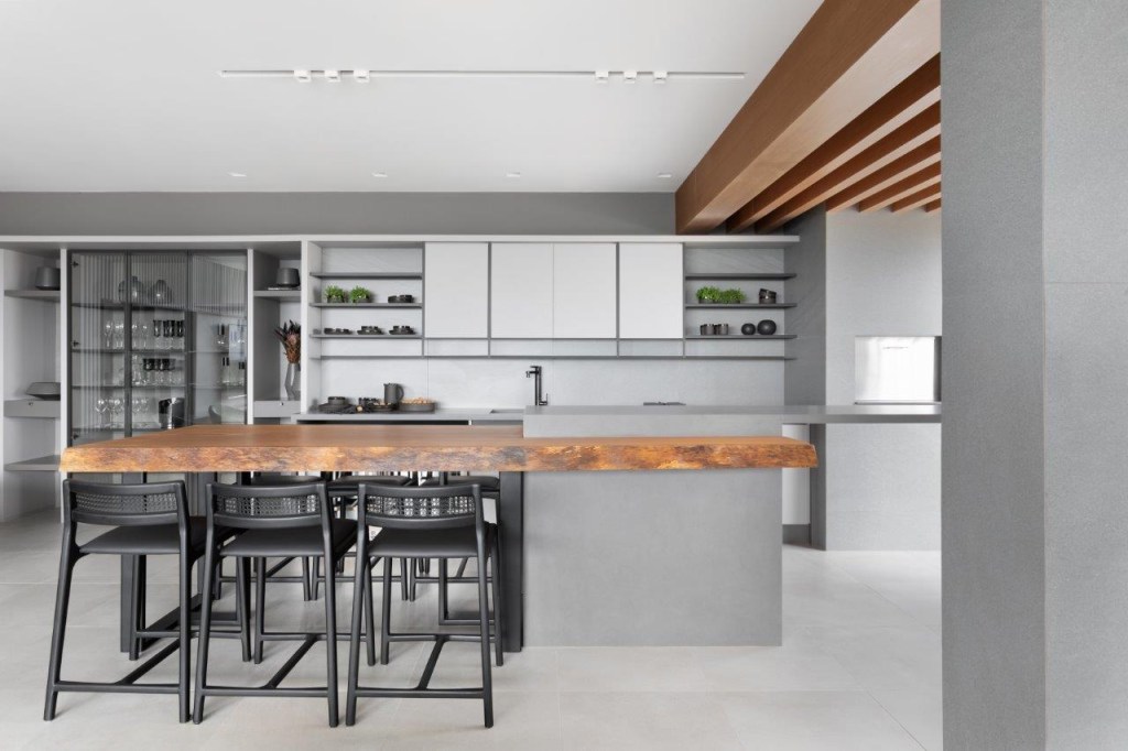 Projeto de archi.lab. Na foto, cozinha americana integrada com marcenaria cinza e ilha com bancada de madeira maciça.