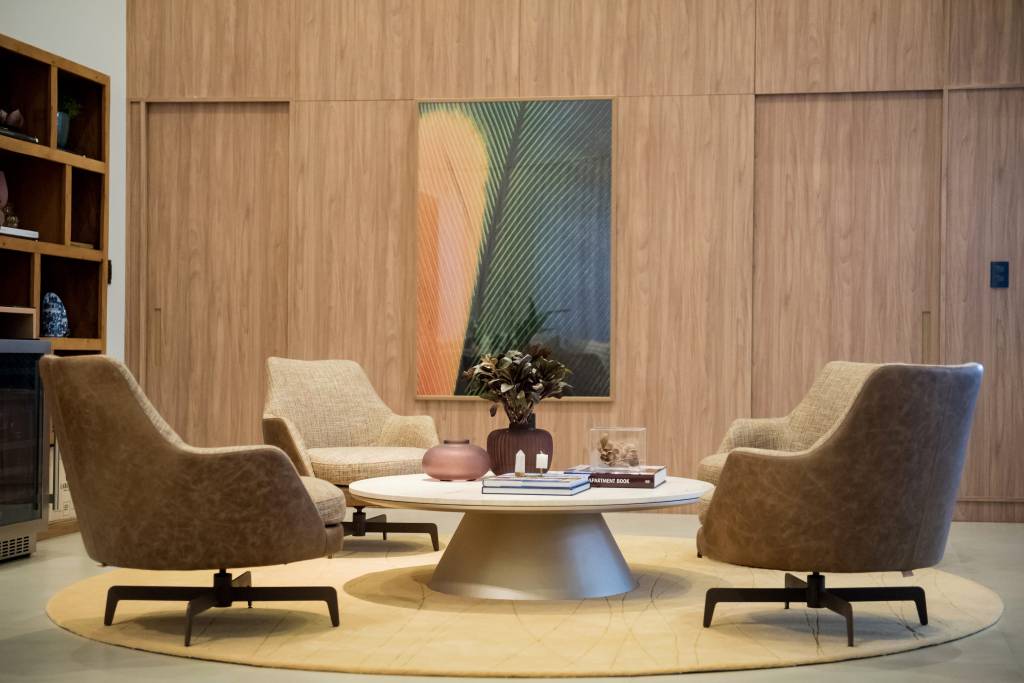 Sala de estar com poltronas beges, mesa de centro com tampo redondo e paredes revestidas de madeira.