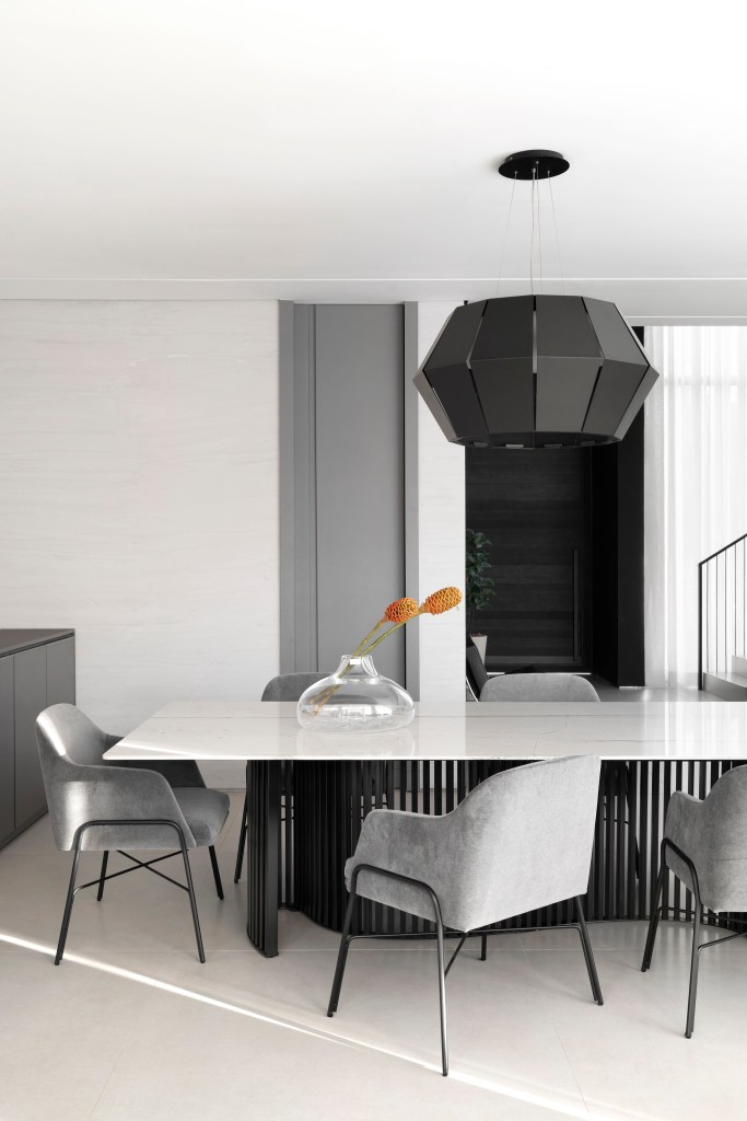 Sala de jantar minimalista com mesa branca, cadeiras cinzas e luminária preta.