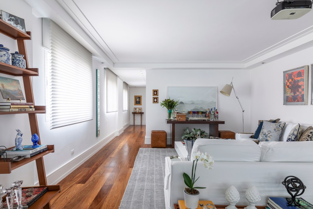 Projeto de Carina dal Fabbro. Sala de estar com piso de madeira, sofá branco e aparador de madeira.