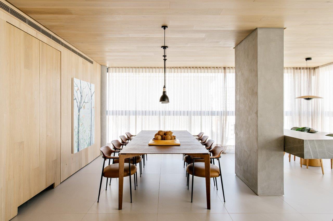 Painéis de madeira revestem o teto e escondem portas neste apê de 220 m². Projeto Très Arquitetura. Na foto, sala de jantar com parede de madeira e quadro.