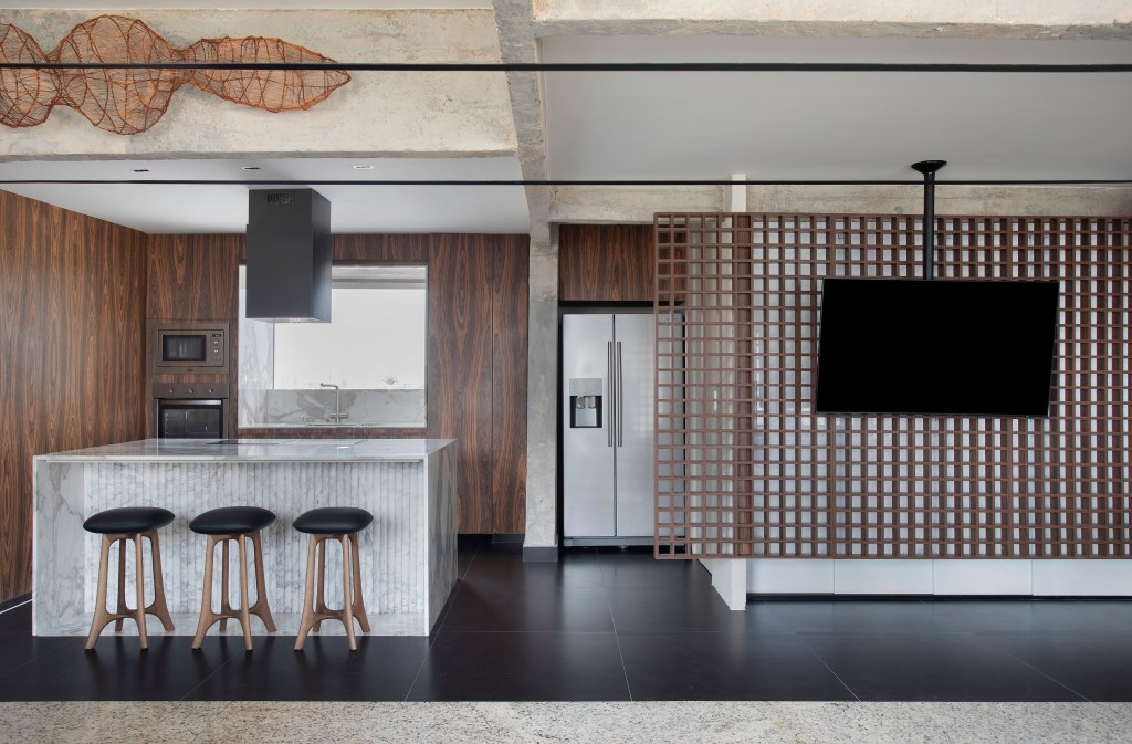 Projeto de Roby Macedo. Na foto, sala integrada com cozinha com painel vazado em forma de muxarabi para tv.