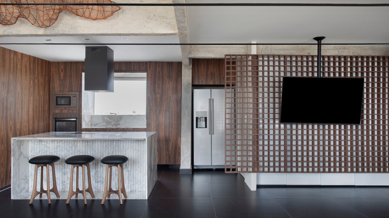 Projeto de Roby Macedo. Na foto, sala integrada com cozinha com painel vazado em forma de muxarabi para tv.