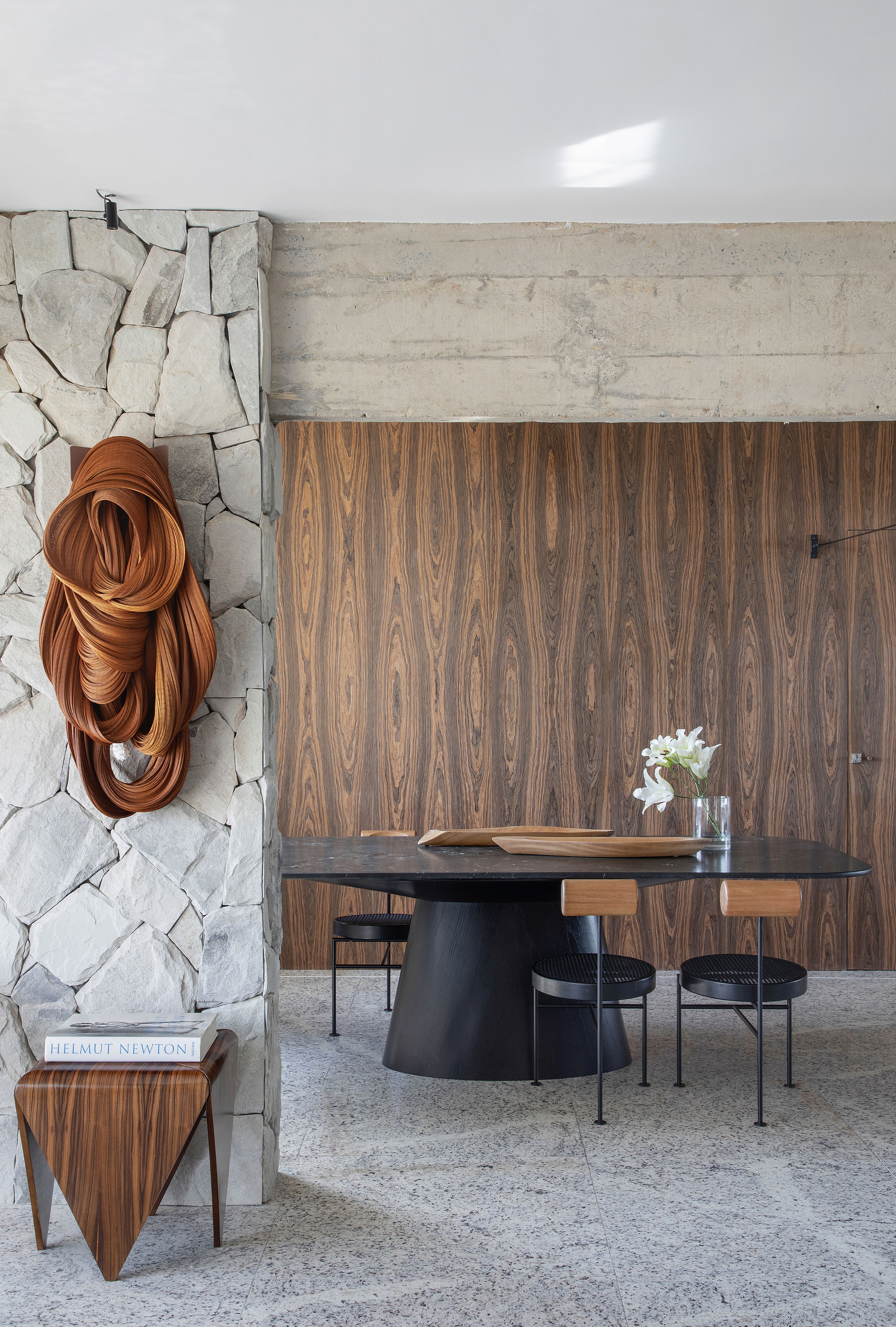 Projeto de Roby Macedo. Na foto, sala de jantar com parede revestida de madeira, teto de concreto aparente e parede de pedra.