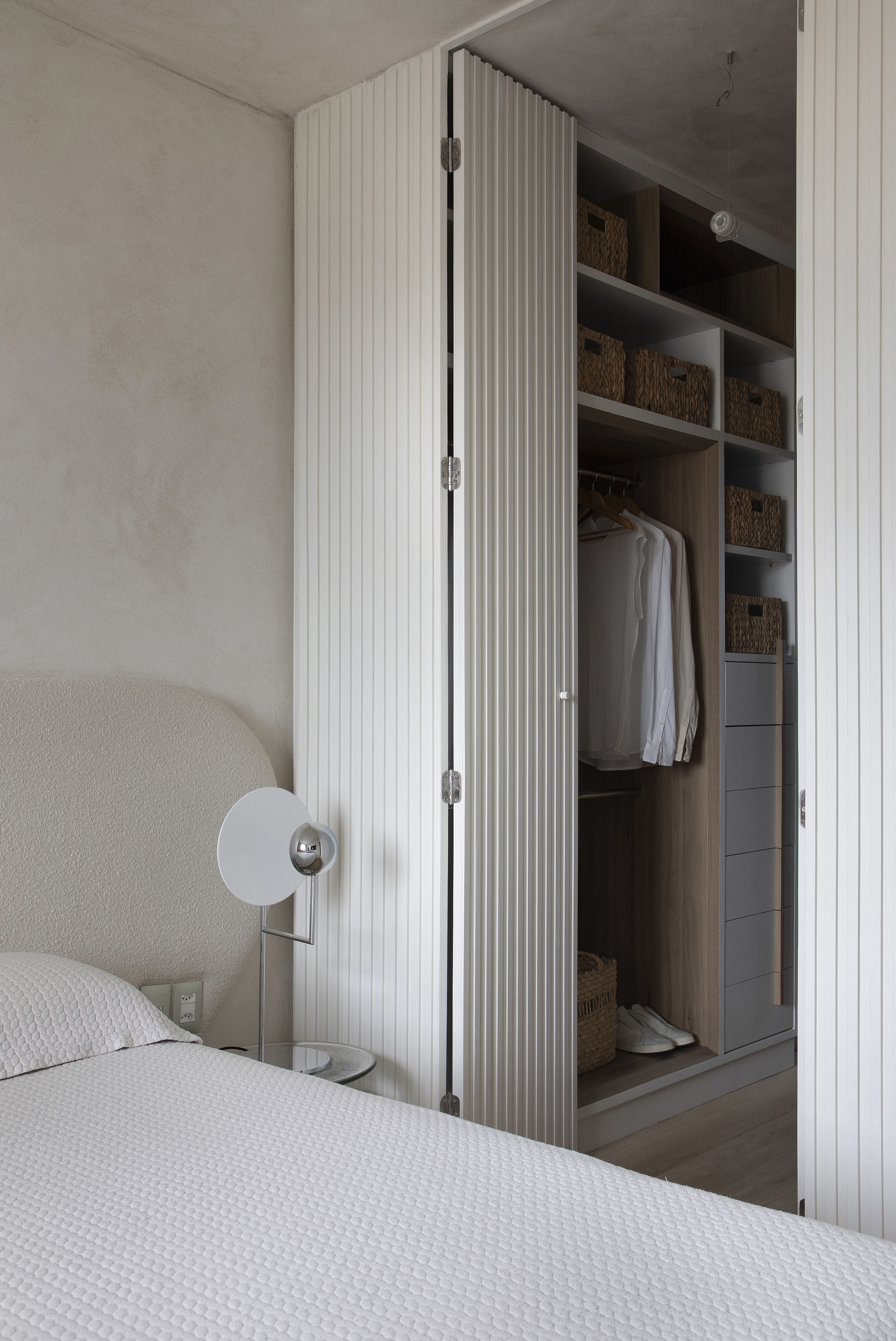 Projeto de Roby Macedo. Na foto, quarto branco com cama de casal e armário com porta de madeira branca ripada.