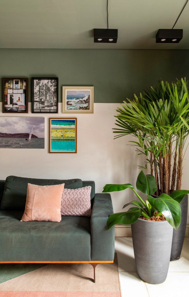 Projeto de Ricardo Abreu. Na foto, sala de estar com sofá verde, vasos de plantas e parede com quadros. Pintura geométrica verde.