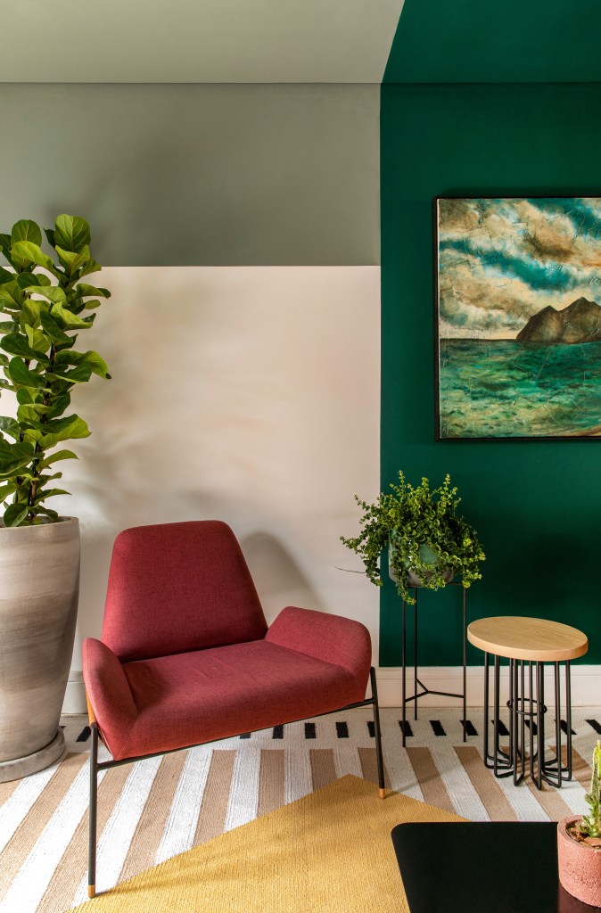 Projeto de Ricardo Abreu. Na foto, sala com poltrona vermelha, parede verde, tapete listrado e planta.
