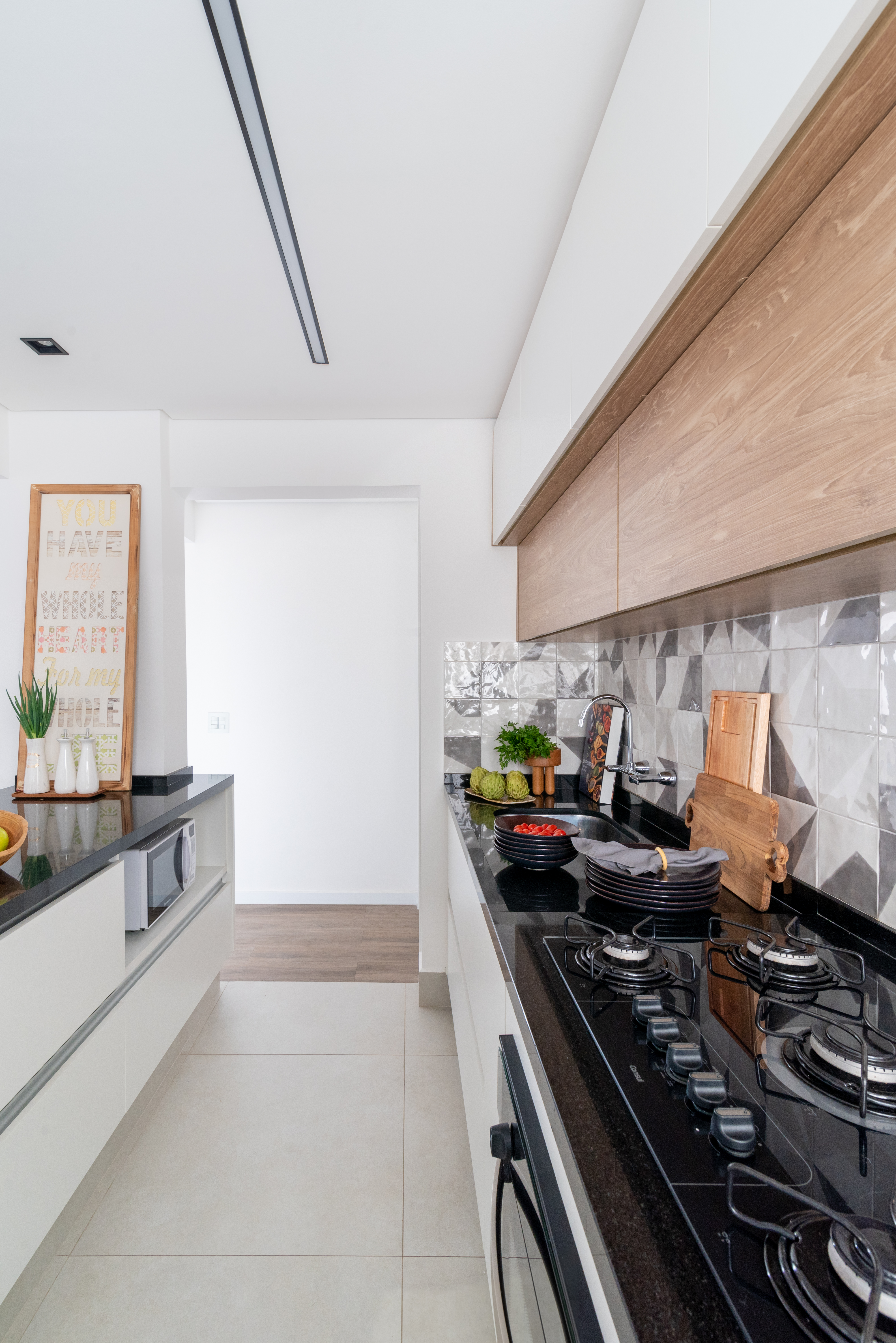 Projeto de Isabella Nalon. Na foto, cozinha integrada com bancada preta e backsplash de azulejos geométricos.