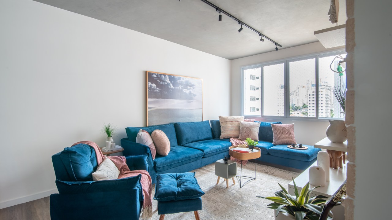 Projeto de Isabella Nalon. Na foto, sala com sofá azul em L, poltrona azul e iluminação com trilho de spot.