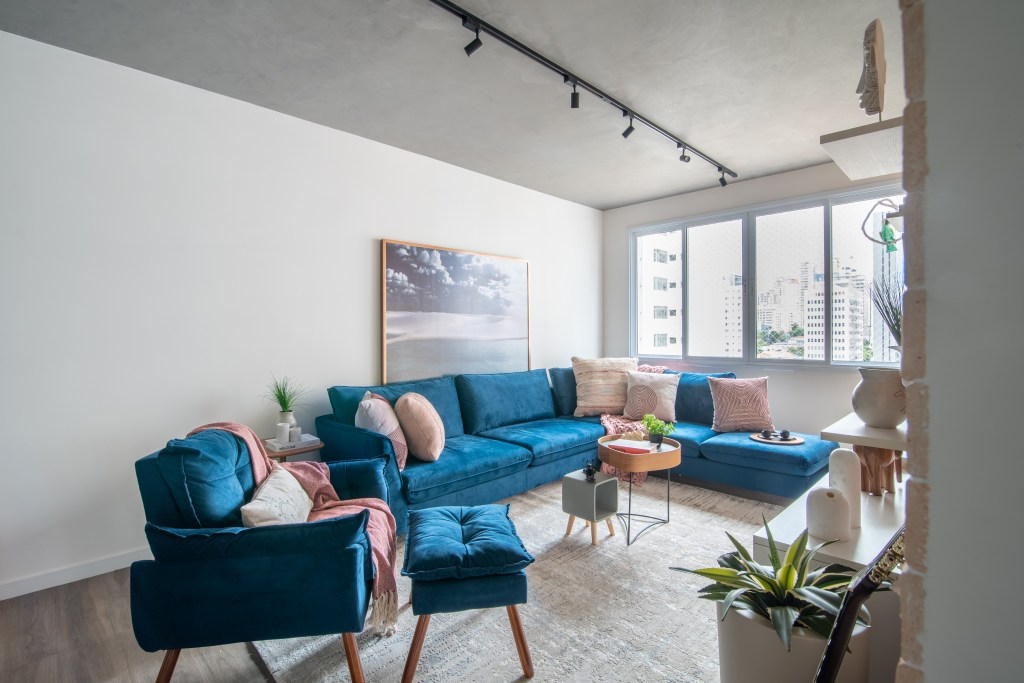 Projeto de Isabella Nalon. Na foto, sala com sofá azul em L, poltrona azul e iluminação com trilho de spot.