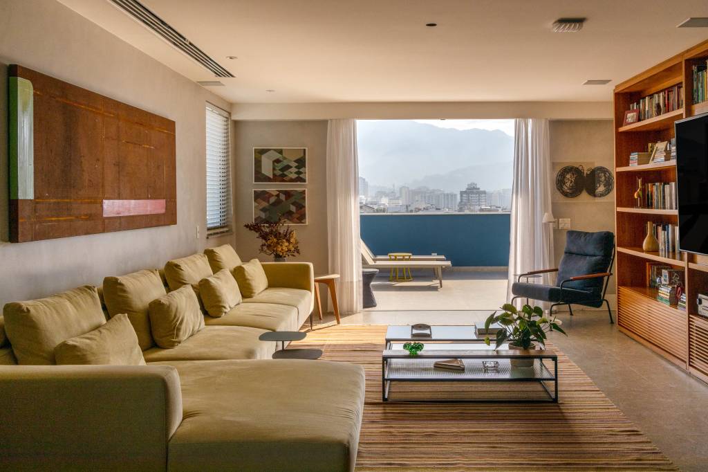 Reforma adapta duplex com vista para o Cristo para família de três adultos. Projeto de Andrea Chicaro. Na foto, sala de tv com sofá em L, estante, quadro e sofá.