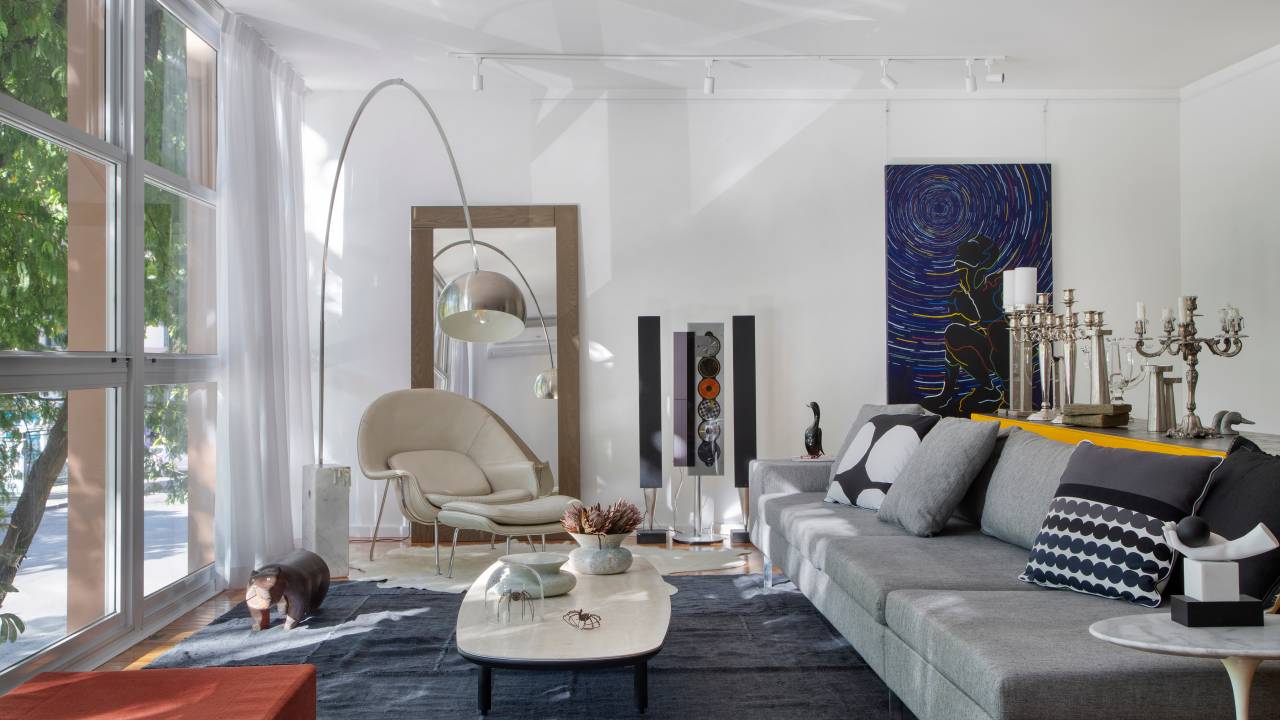 Projeto de Ricardo Melo e Rodrigo Passos. Na foto, sala de estar clara com cortina branca, tapete azul e móveis de design