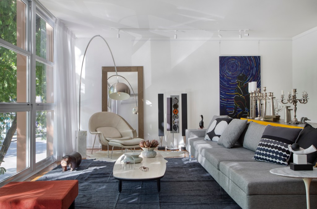 Projeto de Ricardo Melo e Rodrigo Passos. Na foto, sala de estar clara com cortina branca, tapete azul e móveis de design