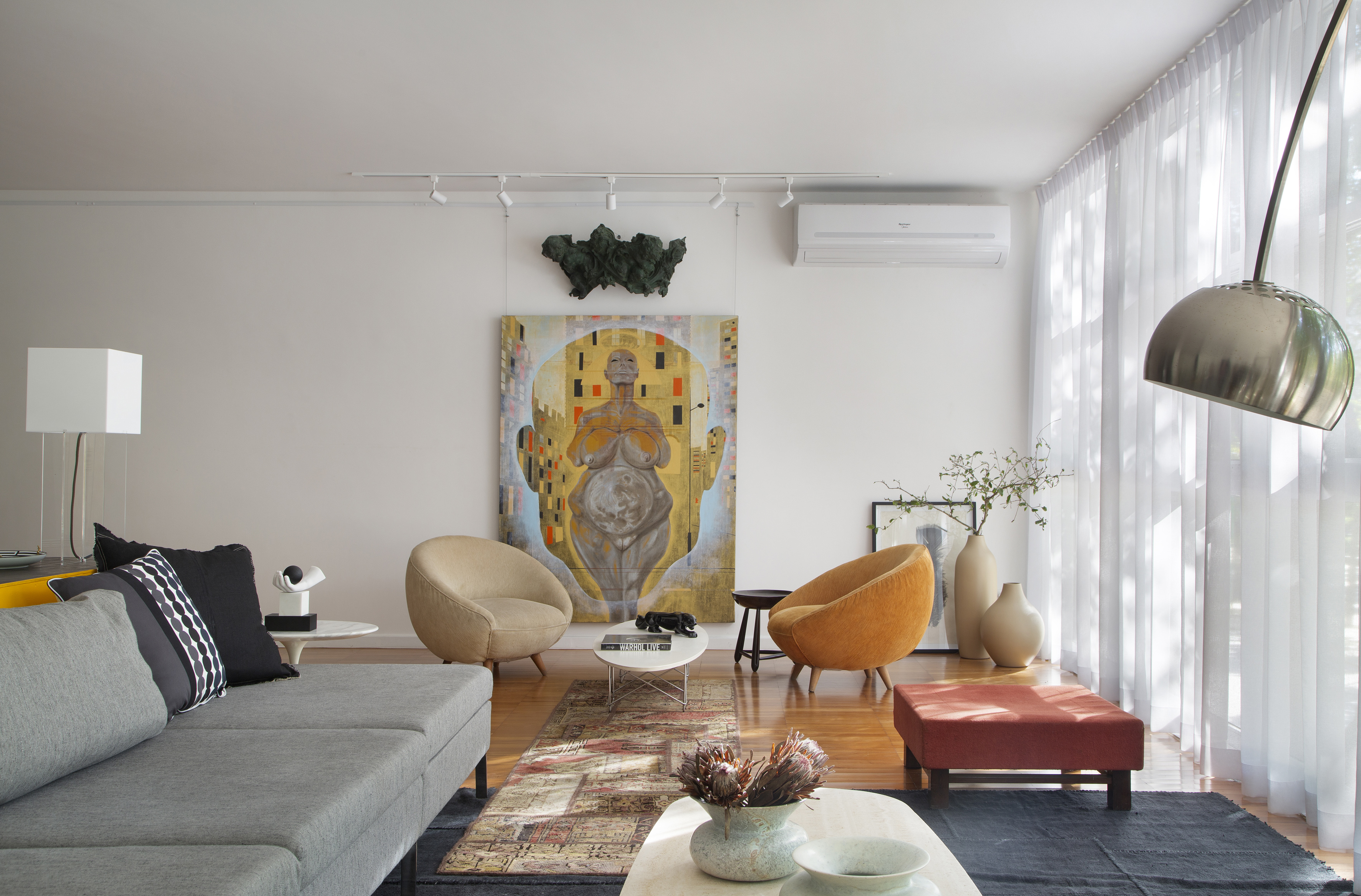 Projeto de Ricardo Melo e Rodrigo Passos. Na foto, sala de estar clara com cortina branca, tapete azul e móveis de design