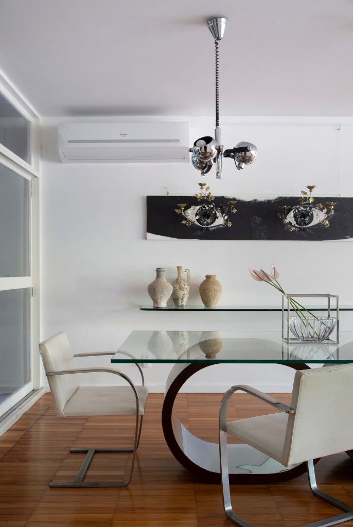 Projeto de Ricardo Melo e Rodrigo Passos. Na foto, sala de jantar com mesa de vidro e cadeira brancas e lustre.