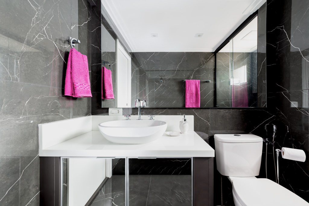 Projeto de Palladino Arquitetura. Na foto, banheiro com revestimento marmorizado preto e louças brancas.