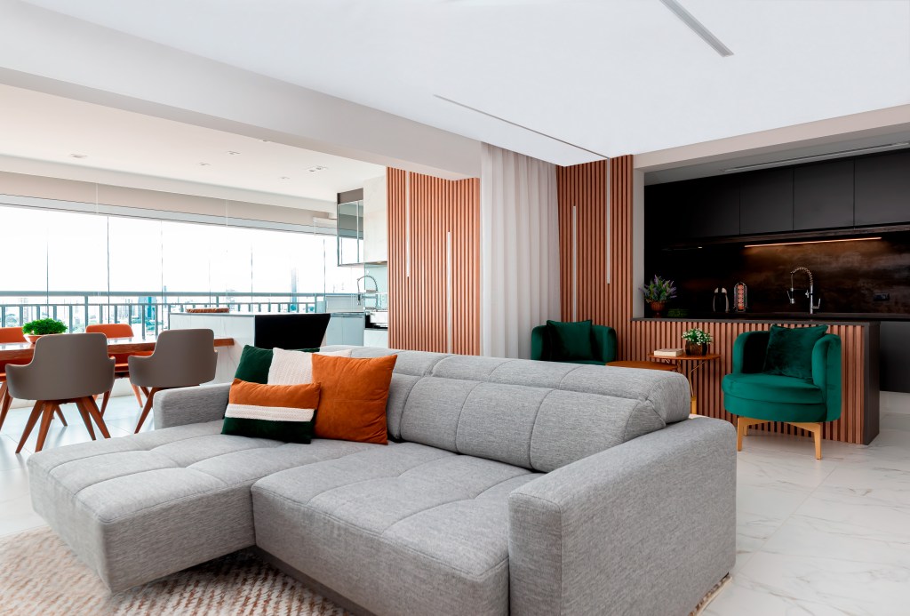 Projeto de Palladino Arquitetura. Na foto, sala de estar com sofá cinza integrada com cozinha e varanda.