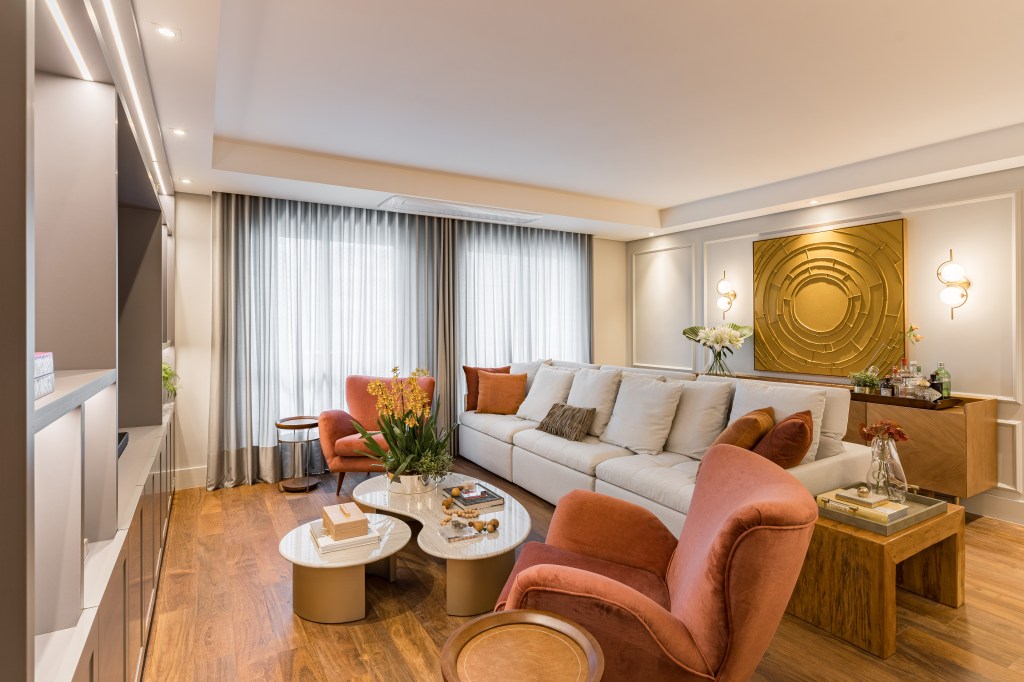 Sala de estar com piso de madeira, poltronas laranja, sofá off white e mesas de centro em formato orgânico.
