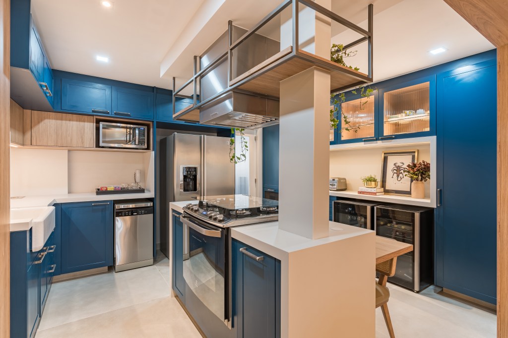 Cozinha com piso de porcelanato, ilha e marcenaria azul; armários com portas de vidro.