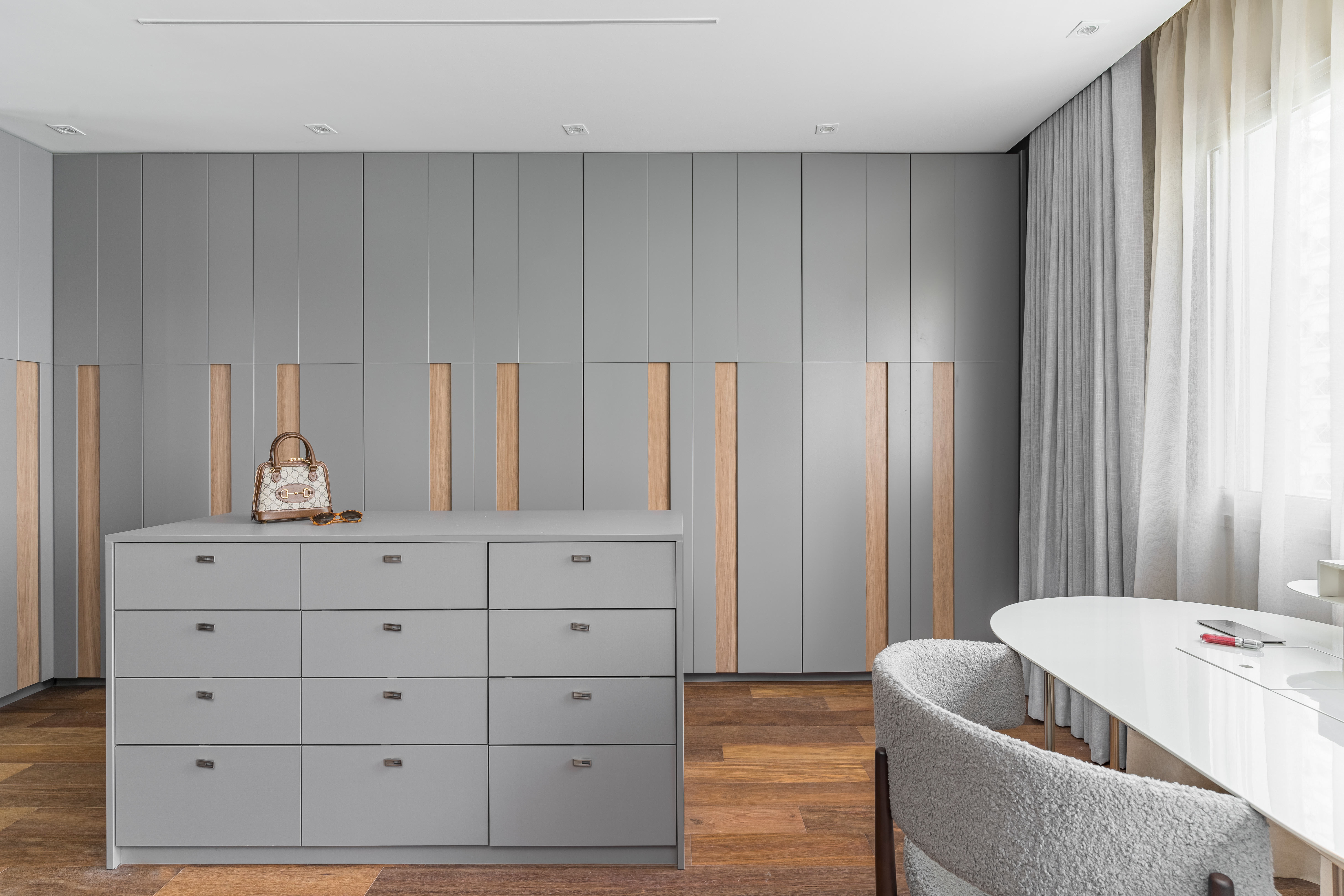 Closet integrado com quarto com armários cinza claros e móvel com gavetas solto.